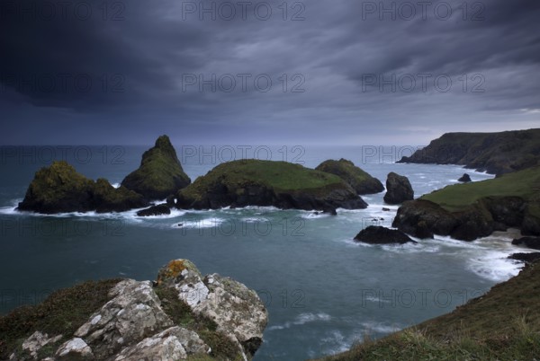 Dramatic clouds on rocky coast, rising rain shower over rocky islands with foaming surf, Kynance Cove, The Lizard, Cornwall, England, Great Britain