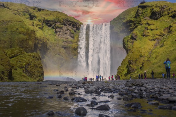 Group of tourists looking at the beautiful rainbow at the impressive Skogarfoss waterfall in southern Iceland, photo taken in summer on a beautiful sunset