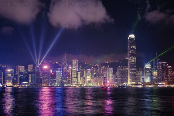 Hong Kong skyline cityscape downtown skyscrapers over Victoria Harbour in the evening illuminated with lasers with tourist boat and ferries, Hong Kong, China, Asia
