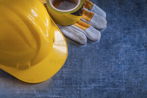 Safety tape yellow building helmet and protective gloves on scratched vintage metallic background construction concept