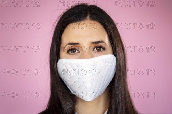 Young woman wearing a protective face mask during the Coronavirus disease COVID-19 outbreak epidemic. Close up portrait with a multiple use white protection mask on the face shot in a studio