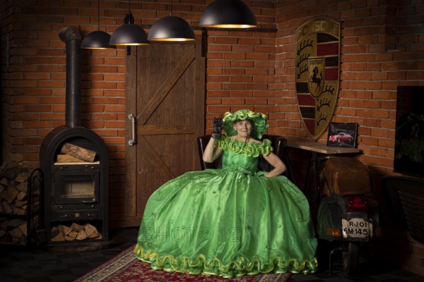 Woman in green dress sitting in a rustic room with fireplace and wood panelling, Staged photo shoot, Mindelheim, Unterallgäu, Bavaria, Germany, Europe
