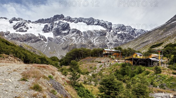 Mountain landscape with snow-covered peak and huts in the foreground on a cloudy day, The landscape near Ushuaia in Argentina