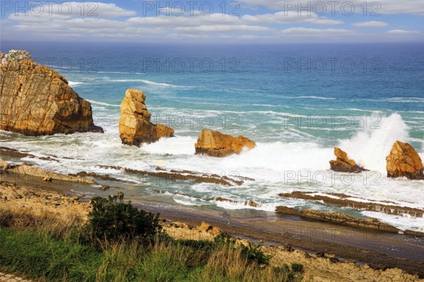 Storm waves break on the coastal rocks. Snow-white sea foam glistens in the dim autumn sun. Playa de la Arnia beach. Cantabria, Spain. Amazing geological formations amaze tourists