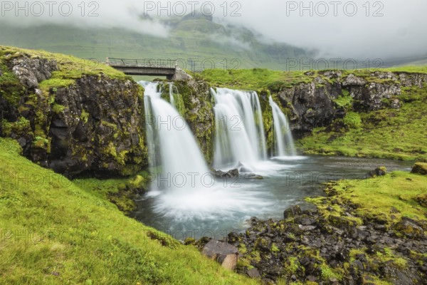 Iceland - country of mountains, rivers and waterfalls. Threaded full-flowing waterfall on the grassy mountains