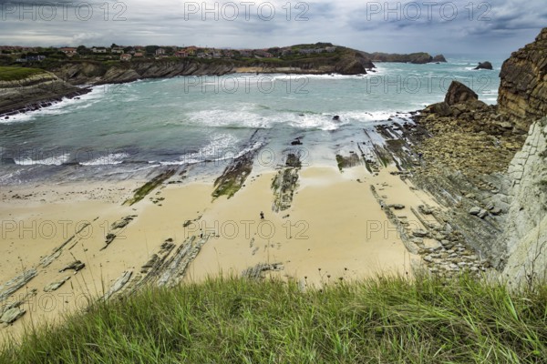 Giant rough gray rocks and smooth sandy beach. Noon on the beach of Playa di Arnia, Spain. Rocky picturesque ocean coast. Cantabria. Windy stormy day on the Atlantic coast