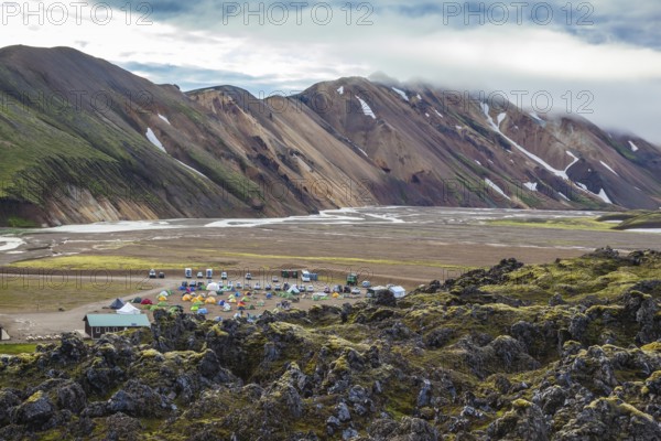 The valley is large tourist camp. Pink and green rhyolite mountains surround the flat valley of the National Park Landmannalaugar