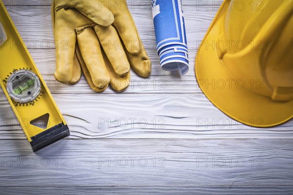 Assortment of working gloves hard hat blue rolled blueprints construction level on wooden board