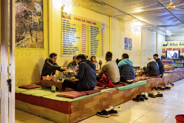 A group of people sit on traditional platforms and enjoy a meal together in a restaurant, restaurant in the streets of Sa Pa in Vietnam
