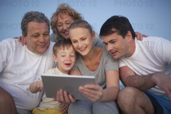 Happy big family having good time together. Grandparents and parents looking at the pad screen while boy using it