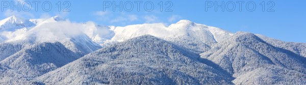 Winter travel vacation nature panoramic background with snow covered mountain peaks and blue sky with clouds closeup