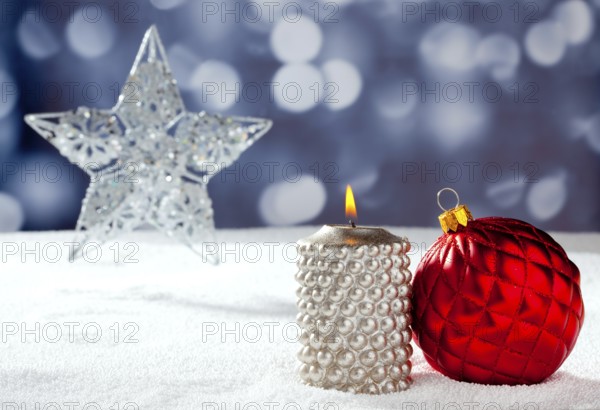 Christmas card of silver star bauble and candle on snow and blue background
