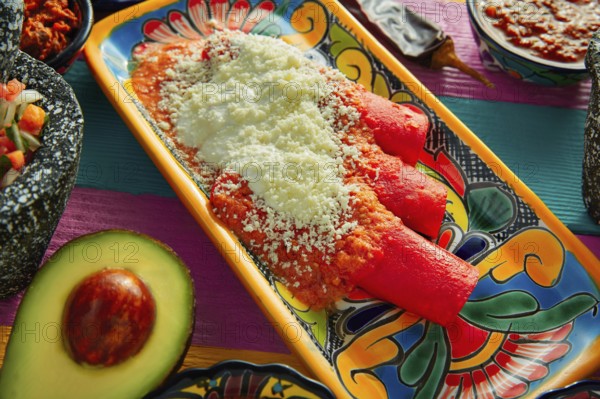 Red enchiladas Mexican food with guacamole and sauces on colorful table