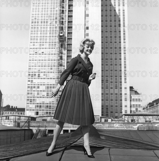 In the 1950s. A woman modelling a 1950s outfit with a jacket and skirt in matching dark. In the background the newly finished skyscraper housing the swedish tax offices. Sweden 1959 Kristoffersson ref CH21