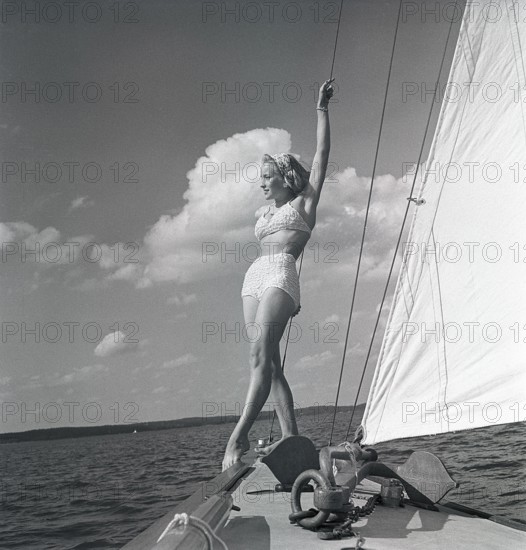 1940s sailing boat. A young woman is aboard a fashionable sailing boat and is standing on deck when it cruises forward with wind in the sails. She is wearing a typical 1940s two piece bathing suit. Sweden 1946 Photo Kristoffersson ref AC101-4