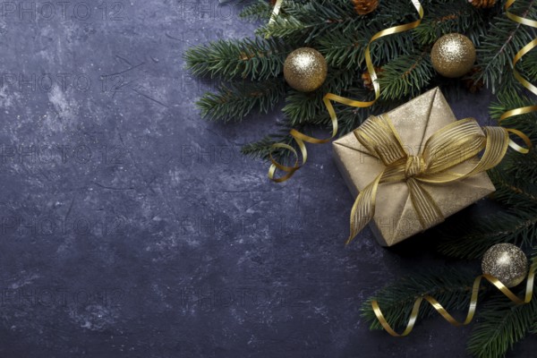 Christmas flat lay with golden gift box and fir tree branch on black stone background with copy space