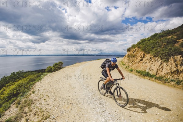 Young guy riding a mountain bike on a bicycle route in Spain. Athlete on a mountain bike rides off-road against the background of the Mediterranean Sea, Costa Brava. Cycling in Spain