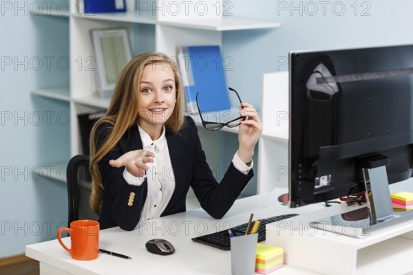 Young pretty business woman sitting at the desk with computer in blue office