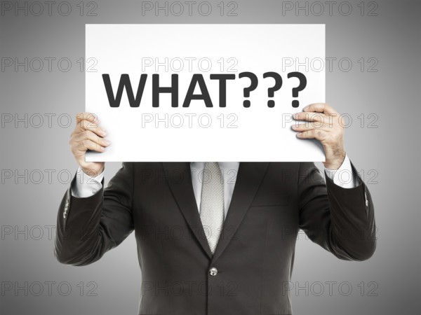 A business man holding a paper in front of his face with the word what
