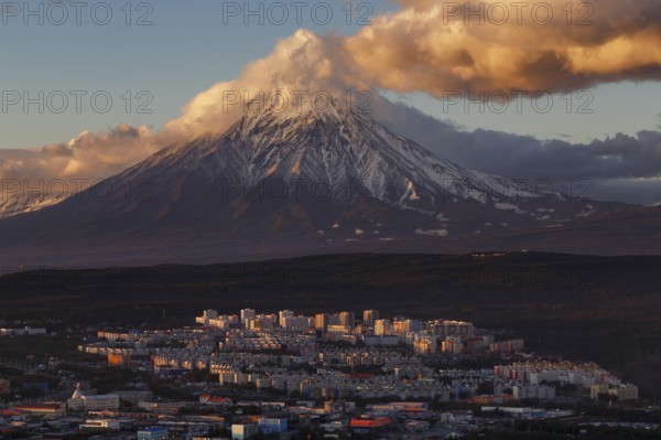 Evening colorful top view of townscape of Petropavlovsk-Kamchatsky City at sunset on background clouds drifting across blue sky, cone of active Koryak Volcano. Kamchatka Peninsula, Russian Far East