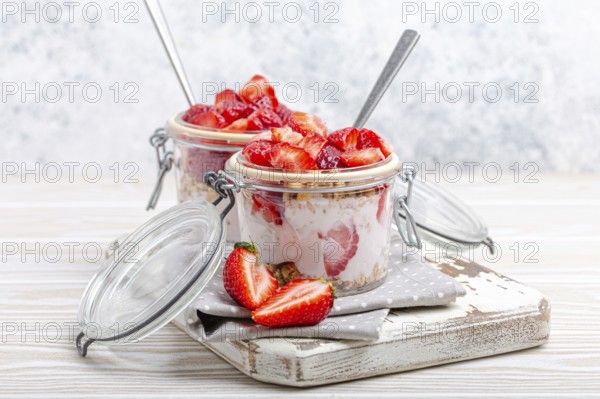 Parfait with Fresh Strawberries, Yoghurt and Crunchy Granola in Transparent Glass Mason Jars on White Rustic Wooden Background from Angle View, Healthy Breakfast or Light Summer Fruit Dessert, food photography, food photography