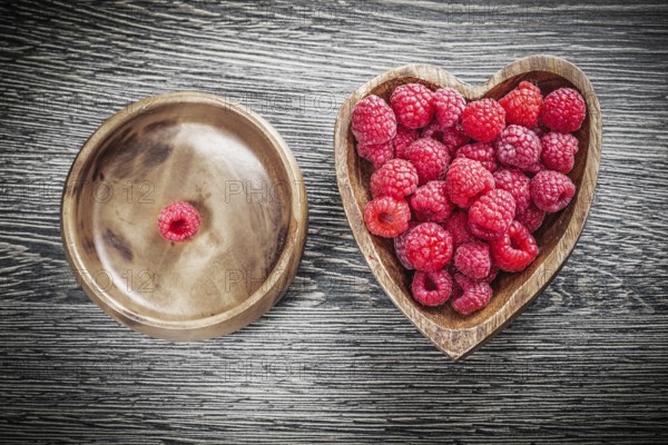 Round and heart-shaped bowls with juicy raspberries on wooden board