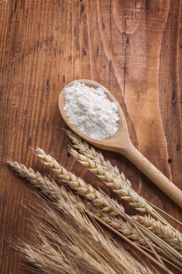 Wooden spoon with white flour and ears of wheat rie on vintage board