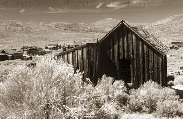 Old wooden shed in Bodie, behind it grassy hills of the prairie. Photo in sepia tone. Old wooden shed in Bodie, behind it graß hills of the prairie. Photo in sepia toning