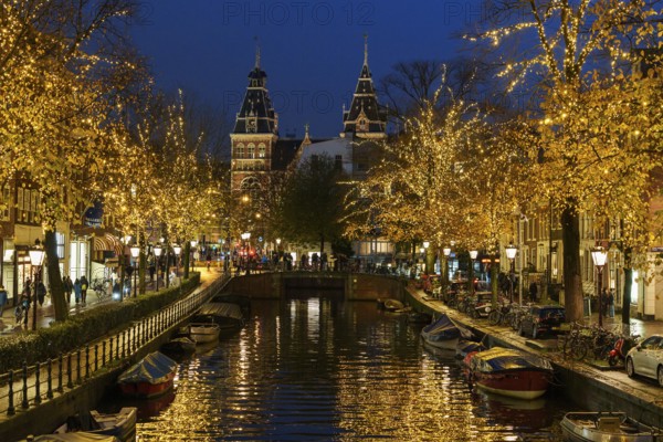 Illuminated canal and bridge at night, surrounded by trees and historic buildings, Amsterdam, Netherlands