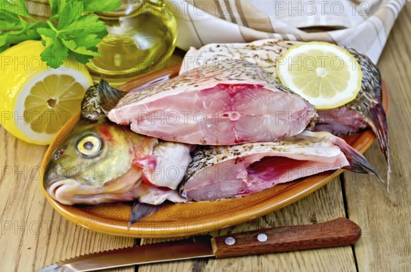 Bream whole peeled and cut into chunks in a clay plate, parsley, lemon, vegetable oil, napkin, knife on the background of wooden boards