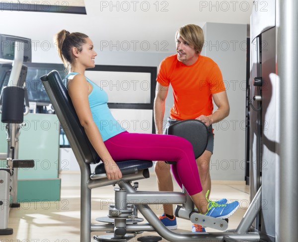 Hip abduction woman exercise at gym indoor closing legs and personal trainer blond man