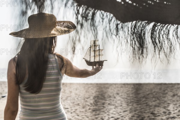 Woman with hat hold boat model on the beach