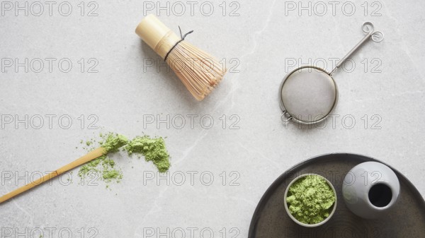 Matcha green tea powder and utensils for drink preparation: traditional bamboo spoon and whisk. Top view on gray stone table