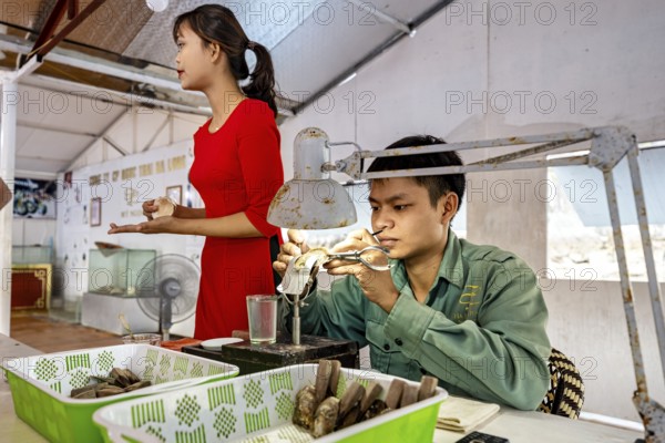 A man concentrates on his work while a woman stands next to him, pearl farm in Halong Bay, Vietnam, Asia