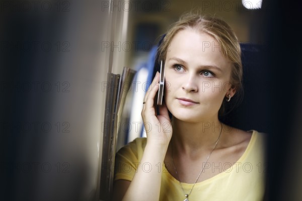 Attractive woman listening to a call on her mobile phone looking into the distance with a thoughtful expression while travelling by train