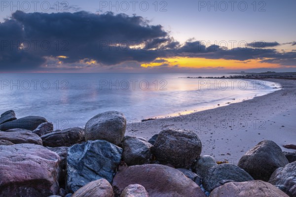 Atmospheric landscape at the seaside at sunrise with big stones in the foreground. Big stones at the seaside in long exposure photography