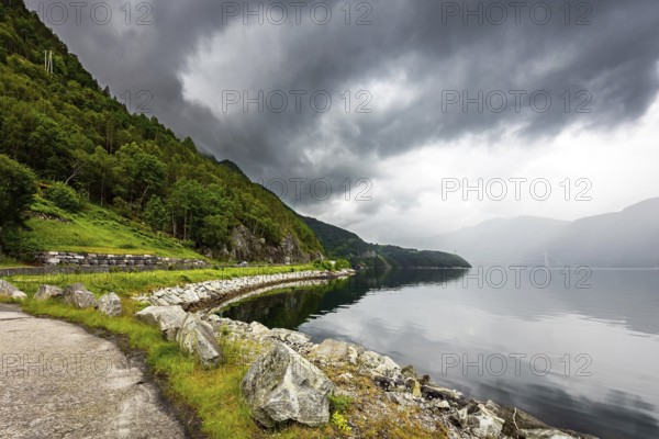 Scenic road in the mountains of Western Norway. Beginning of the Hardangerfjord. Scandinavia. Summer. Powerful clouds are reflected in the water surface of the fjord