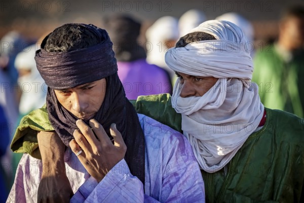 Two men in traditional dress and turbans, one puts his arm around the other, The traditional Tuareg at the Tamanrasset Festival in the Sahara in Algeria
