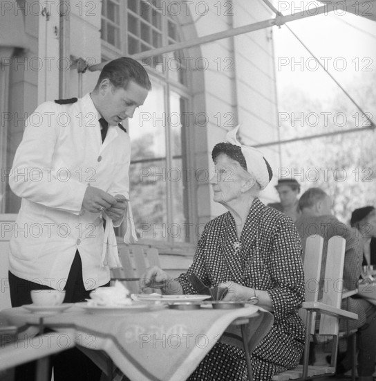 1950s restaurant. An elderly lady is having a conversation with the waiter when settling the bill. Sweden. Photo Kristoffersson BX30-6. Sweden 1956