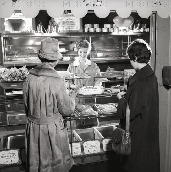 1960s coffee shop. Two women are standing in front of the counter that is full with freshly baked cakes and pastries. Sweden 1960s ref CX80-3