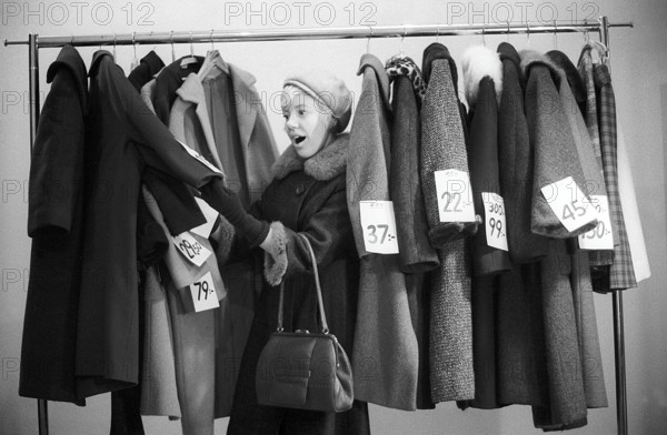 Great discounts of outerwear in the 1960s. A woman stands by a clothes rack, choosing from outerwear and coats marked with price tags with discounted prices. Judging by her face, she appreciates the reduced prices and thinks she's getting real bargains. Sweden January 1963. Ref CV28
