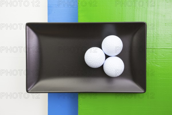 Black ceramic dish with golf balls on over white, blue and green wooden table, rectangle dish