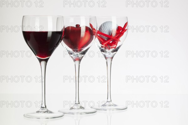 Wine glasses with red wine, heart and golf ball on white table