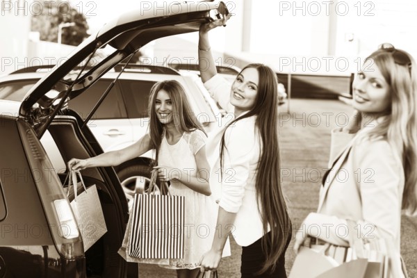 Group of girls after shopping loading a shopping bags in a car trunk