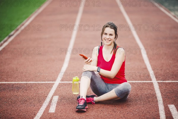 Beautiful fitneß girl uses smartphone at stadium after workout. Sports and healthy. Sport woman use of cellphone inside sport complex. Sport and technology. resting after workout, run at red track