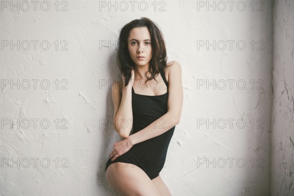 Portrait of ayoung sports woman of athletic build in swimsuit. Woman spend time in a dance studio. Beauty Woman In Sport Wear Stand On Wall. bodysuit posing on wall background. Girl with no makeup