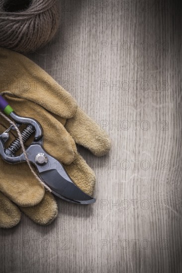 Pair of leather safety gloves sharp metal secateurs and skein of twine on wooden background agriculture concept