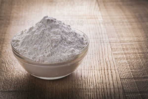 Transparent glass bowl with white natural flour on vintage wooden board food and drink still life