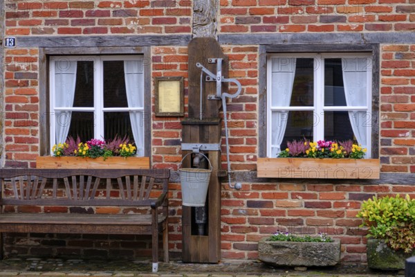 Brick wall with two windows and flower boxes, next to it a wooden bench, gemen, münsterland, germany