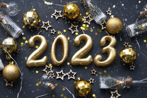 The golden figures 2023 made of candles on a black stone slate background are decorated with a festive decor of stars, sequins, fir branches, balls and garlands. Greeting card, happy New Year